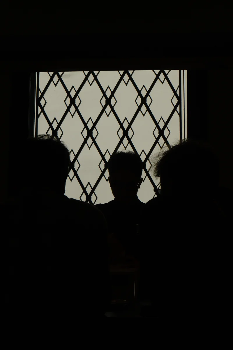 Silhouettes gather around a counter beneath a patterned window.