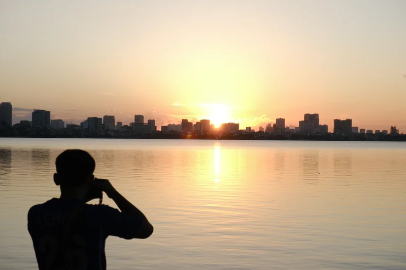 A photographer catches the last sunlight across the water in Hanoi.