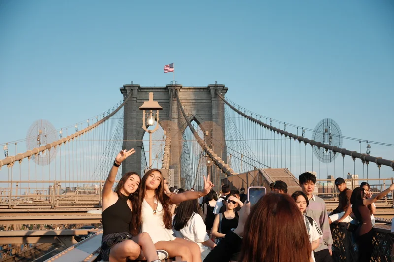 Visitors pause for photographs on the Brooklyn Bridge in the warm evening light.