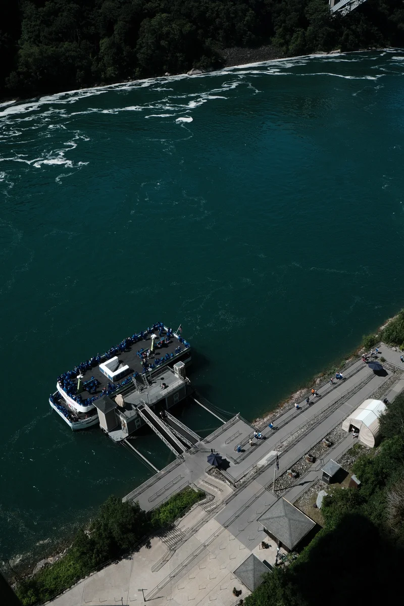 A sightseeing boat rests beside a landing at the edge of deep green water.
